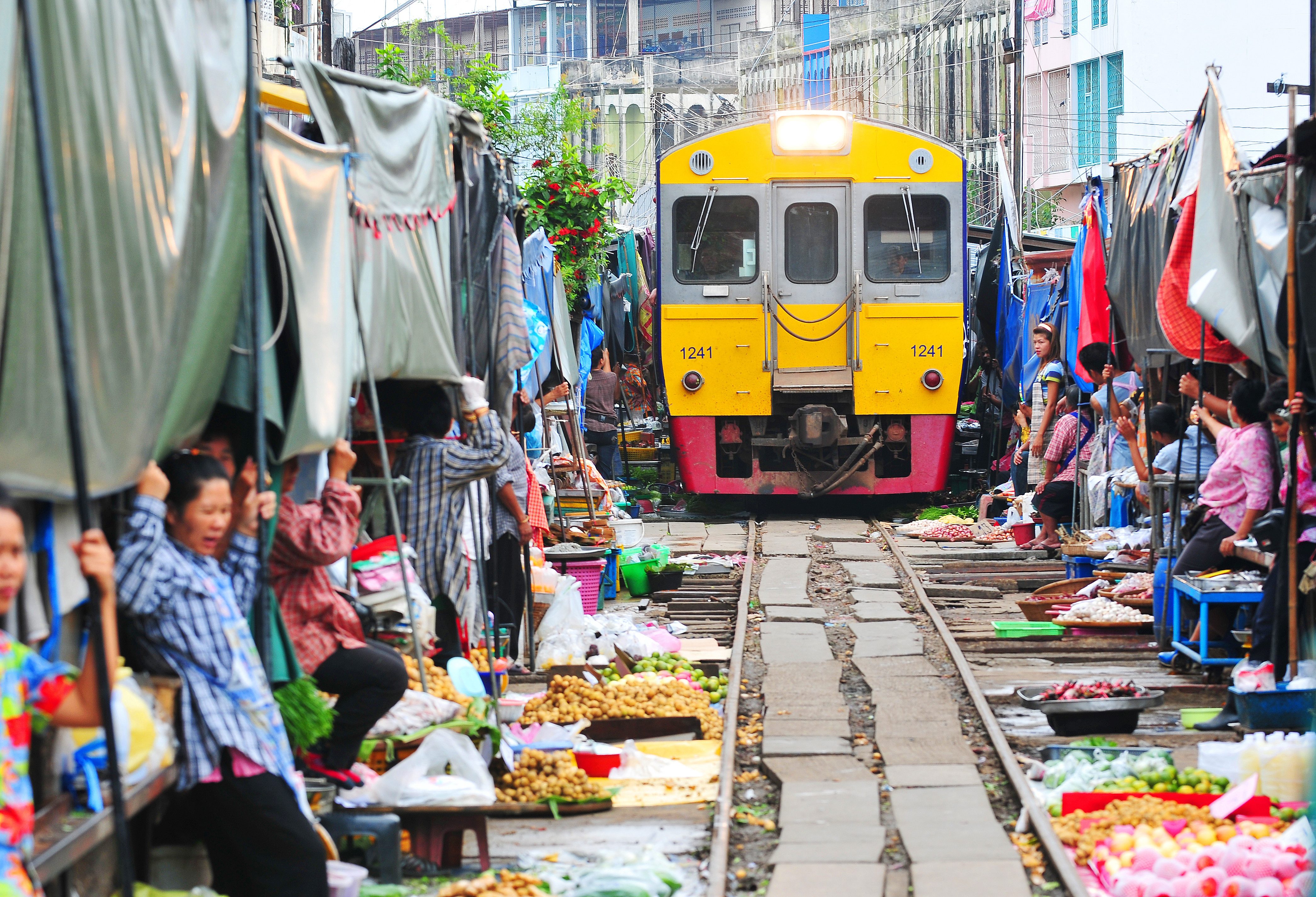 Trein rijdt vlak langs huizen en koopwaar in Thailand
