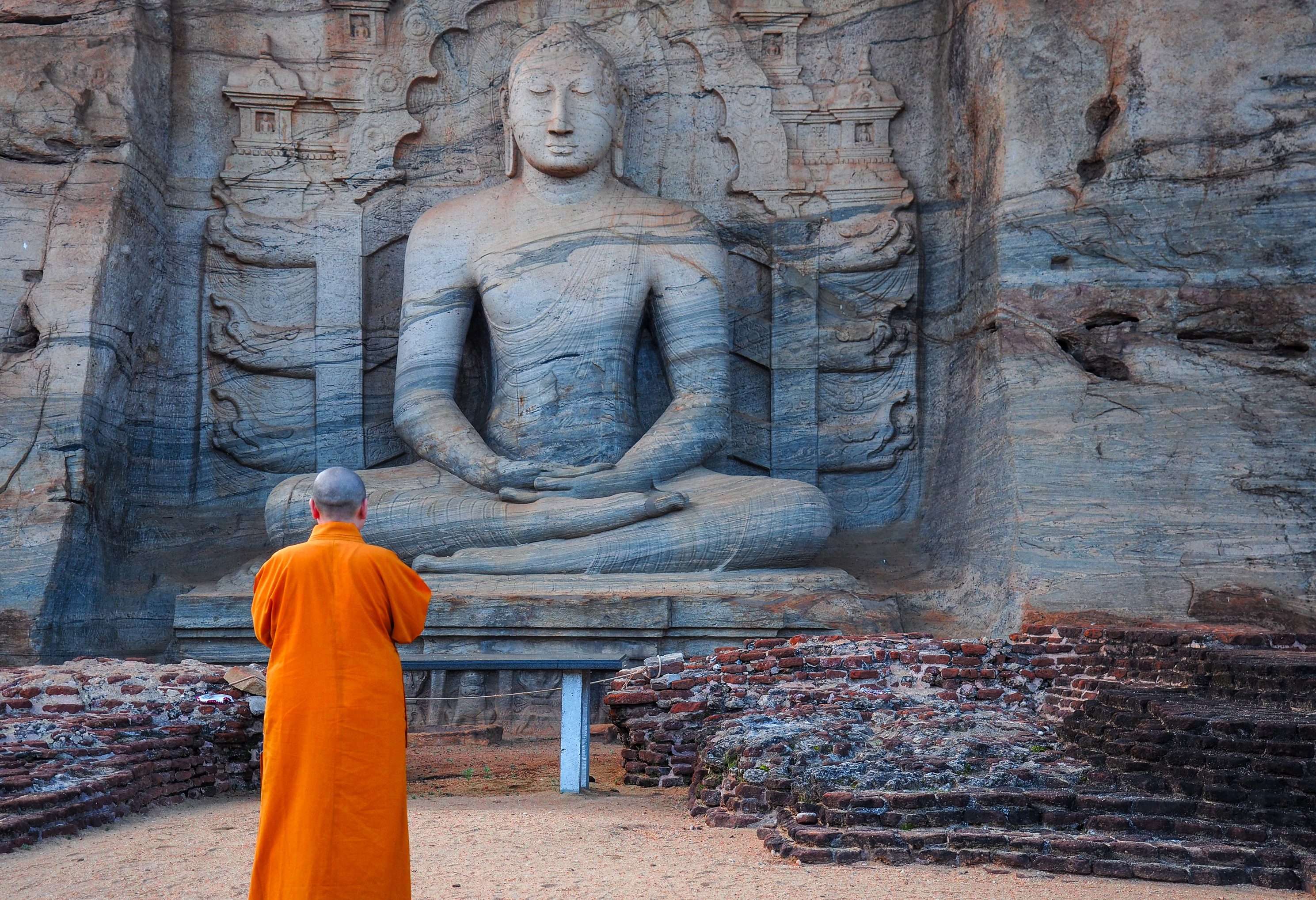 Monnik bij zittende Boeddha in Polonaruwa